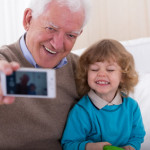 Smiling grandfather with grandson taking photo by mobile phone